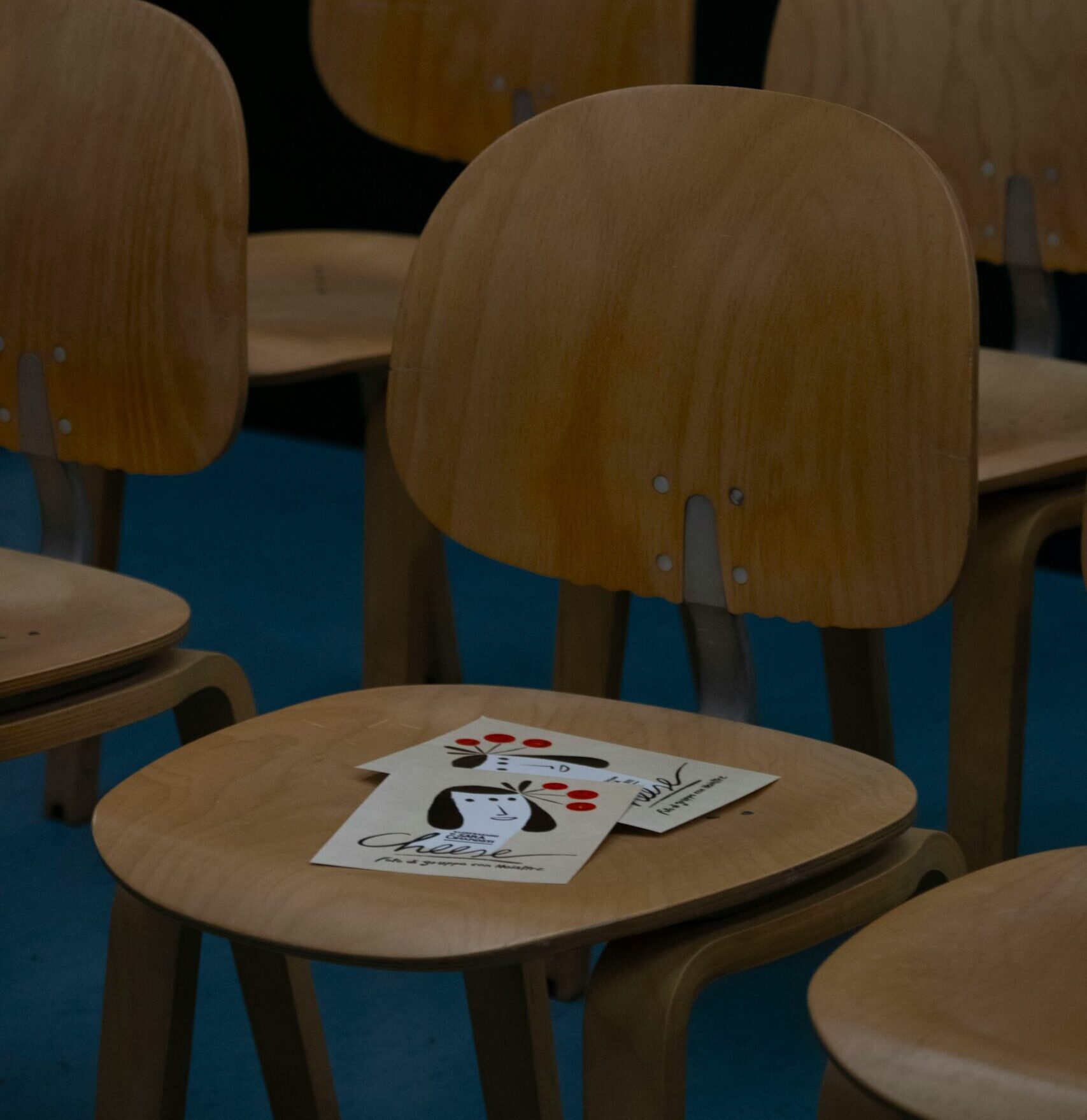 wooden chairs are arranged with some papers on one